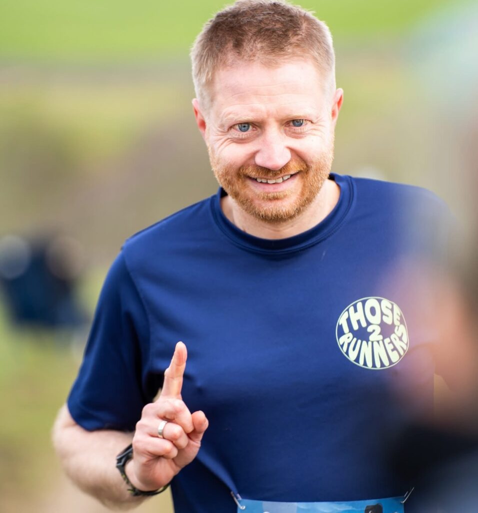 Chris holding up one finger to represent first place. He wears a Keep On Running t-shirt